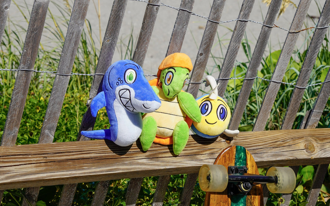 A Coral Reef Crew plushie with a skateboard by the beach fence